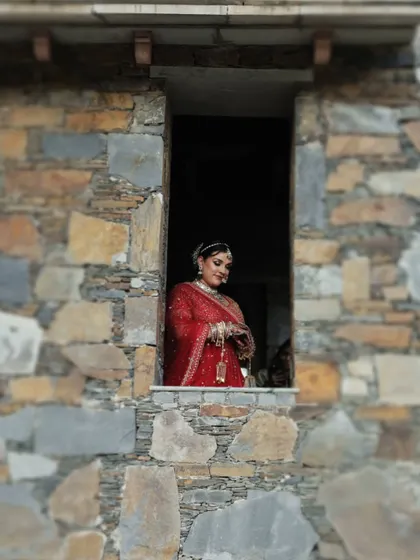 The bride is framed within a rustic stone window, creating a classic, painting-like portrait.