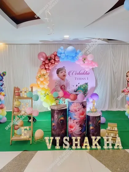 A full stage setup for a Krishna themed first birthday, including character props, themed cake stands, and marquee letters.