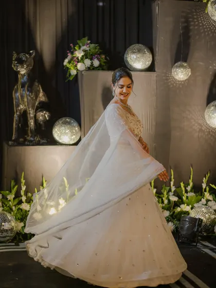A dreamy, twirling shot in a shimmering white lehenga, surrounded by disco balls and floral decor. Perfect for a glamorous sangeet night.