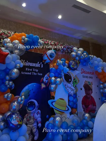 A close-up of the backdrop for Shivansh's "First Trip Around The Sun." The space theme is detailed with astronaut and planet cutouts, personalized banners, and a galaxy of blue, orange, and silver balloons.