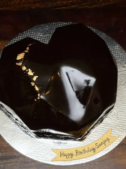 A sleek and sophisticated heart-shaped mousse cake with a dark chocolate mirror glaze. The glossy finish is so reflective you can see your face in it, and the gold leaf adds a touch of luxury.