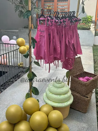 A unique display of personalized aprons for a pizza-making party. The pink aprons are hung on a tree-like rack, adding a creative and functional element to the decor.