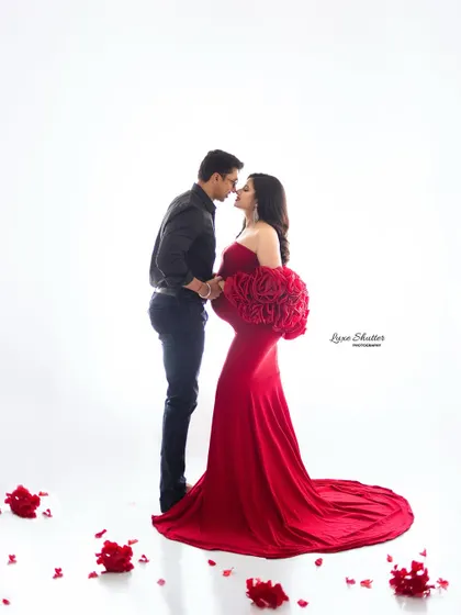A romantic and powerful silhouette. The couple shares an intimate moment, framed by the bold red of the gown and scattered rose petals.