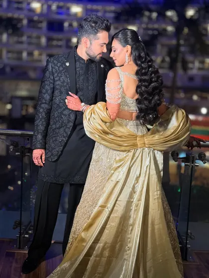 A romantic couple shot on a balcony, showcasing the bride's magnificent golden gown and glamorous makeup.