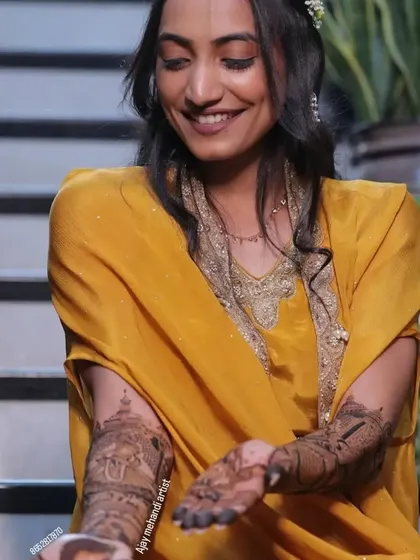 A smiling bride looking down at her hands, admiring the beautiful and detailed story-telling mehndi I created for her.