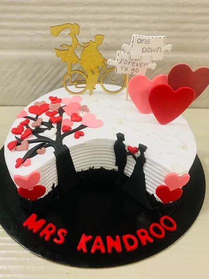 A sweet and romantic anniversary cake telling a love story. It features a silhouette of a couple under a tree of hearts and a topper that says "one down, forever to go."