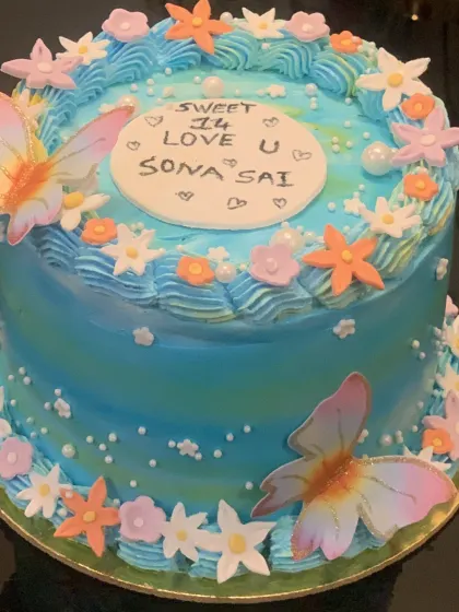 A vibrant blue cake decorated with colorful flowers and butterflies. The handwritten message adds a personal touch.
