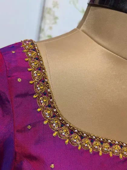 A close-up of the neckline of a pink and purple dual-tone blouse, featuring a meticulously embroidered border.