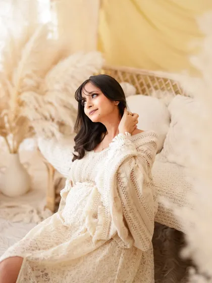 A duplicate of image 2, this dreamy, light-filled portrait captures a mom-to-be in a soft, cream-colored knit dress, surrounded by a beautiful boho setup.