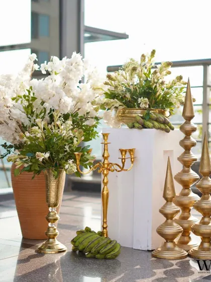 A luxurious arrangement of white flowers in golden vases, paired with modern, sculptural golden candlesticks, creating a look of minimalist opulence.