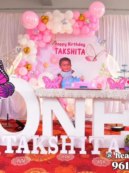 A first birthday setup combining butterfly and fairy elements, featuring a large "ONE" table for the cake. The decor includes fairy wing cutouts, a personalized backdrop, and a pink and white balloon arrangement.