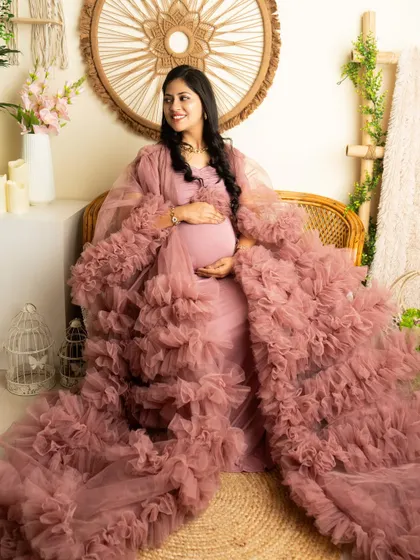 A relaxed seated portrait in a dusty pink ruffled robe. The boho-chic setup creates a comfortable and stylish atmosphere.