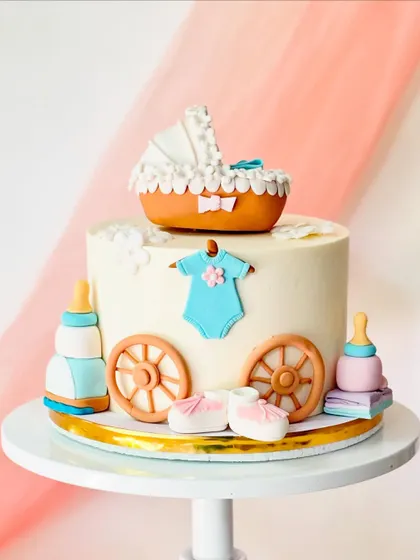 A charming baby shower cake designed to look like a baby carriage. It features a pram topper, a baby onesie, booties, and feeding bottles.