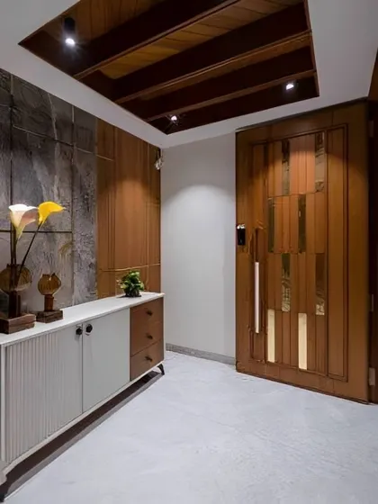 This entryway features a beautiful wooden door with metallic inlays, a stone accent wall, and a sleek console table. The design feels modern and grounded.