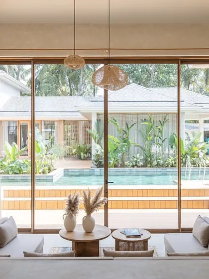 A direct view of the sunken living area in the House of Basho, looking out towards the pool and garden. The large glass opening and low-slung furniture create an uninterrupted connection with the tropical landscape.
