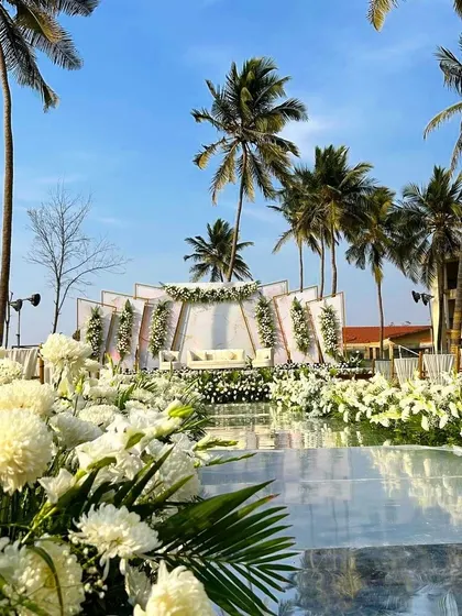 A low-angle shot of the all-white beach wedding, highlighting the mirrored aisle and lush floral decor.