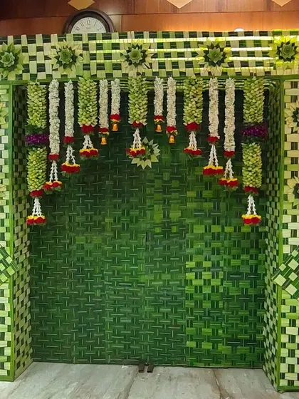 A beautiful and eco-friendly backdrop made entirely from woven coconut leaves. The design is accented with hanging floral garlands, perfect for a traditional pooja or housewarming.