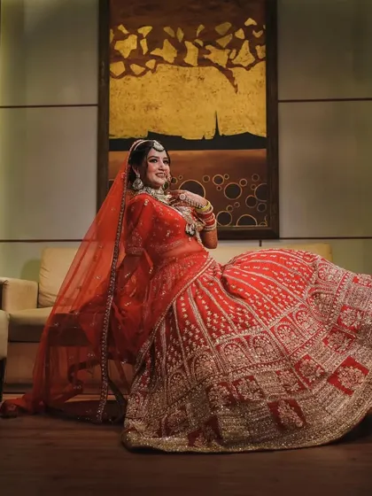 A full-length portrait of the bride seated, her magnificent red lehenga spread around her. This shot emphasizes the grandeur and regality of her bridal outfit.