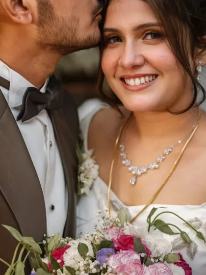 A sweet and intimate close-up. The groom's kiss on her forehead and her serene smile make for a beautiful, romantic photo.