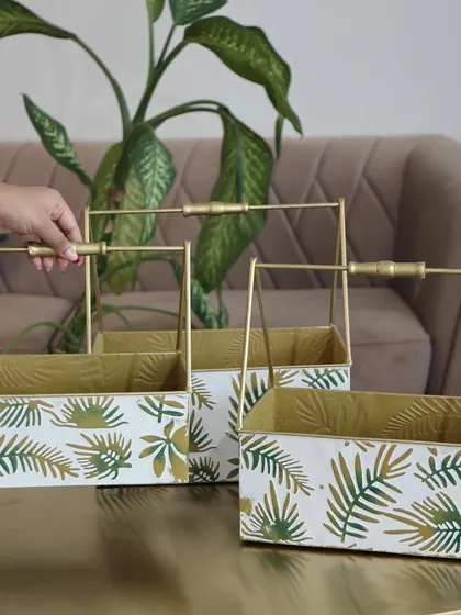A set of three metal baskets with a white and green leaf print and elegant gold handles. These are perfect for organizing your home or as a stylish base for a gift hamper.