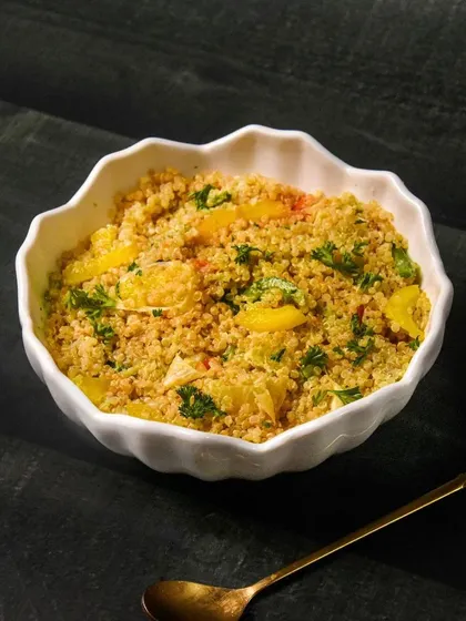 A simple and nutritious quinoa salad with yellow peppers and fresh parsley, presented in a white bowl on a dark table.