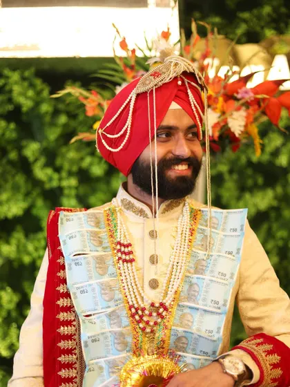 A portrait of a smiling Sikh groom in his traditional wedding attire, complete with a garland of money.