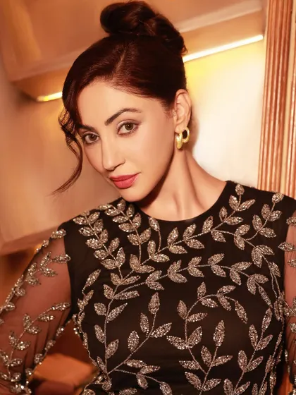 An elegant evening wear shot for a fashion label, featuring actress Reyhna Pandit. The warm, ambient lighting complements the sophisticated, embroidered black dress.