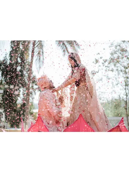 A shower of petals rains down on the couple during their jaimala. This action shot captures the festive and celebratory atmosphere of the wedding ceremony.