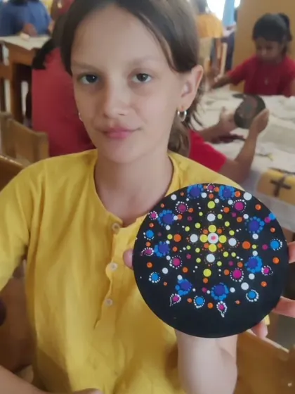 A close-up of a student with her finished dot painting. The intricate pattern and color combination she chose are a testament to her focus and creativity during the school workshop.