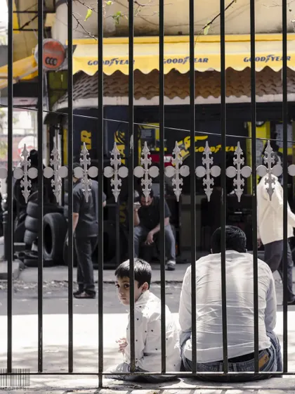 A child looking through a gate. The bars of the gate frame his face, drawing attention to his curious expression. This is an example of using the environment to create a compelling composition.