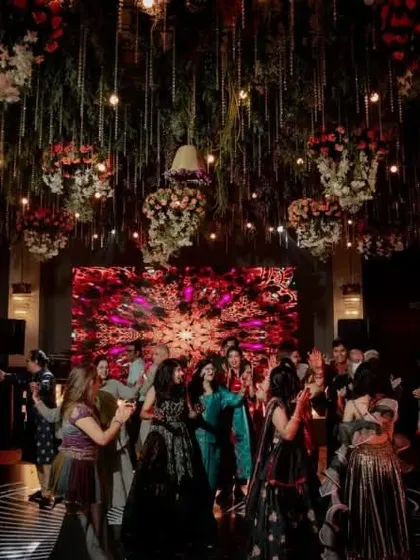 A high-energy Sangeet night with a ceiling full of hanging floral arrangements, disco balls, and fairy lights, creating a magical forest feel.