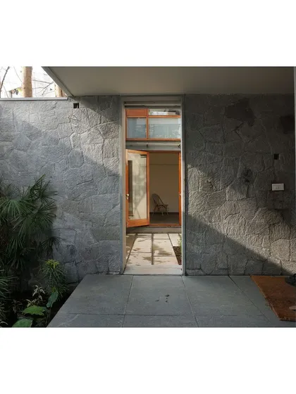 A doorway in the RT Nagar residence is framed by a beautiful, rough-textured stone wall. The contrast between the natural stone and the clean opening creates a powerful entrance.