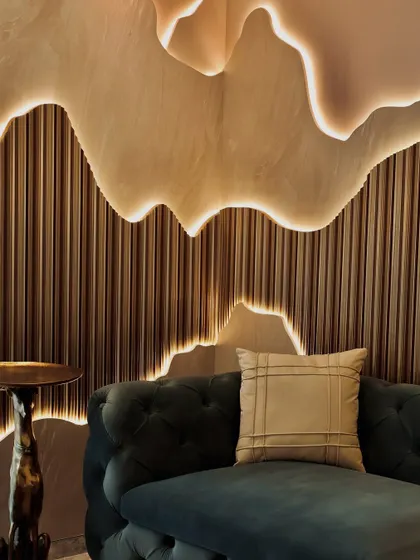 This corner detail highlights the craftsmanship of the illuminated wall feature. The organic, layered shapes and ribbed wooden texture below create a dynamic interplay of light, shadow, and material that adds depth and character to the room.
