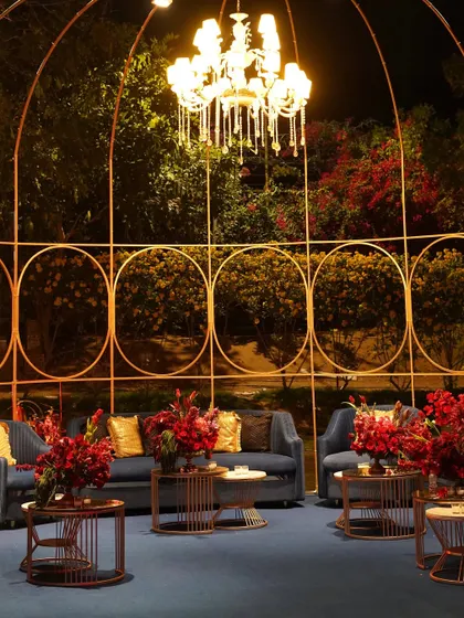 An open-air gazebo lounge for the Sangeet, where a crystal chandelier hung from a simple frame, illuminating a cozy seating area below.