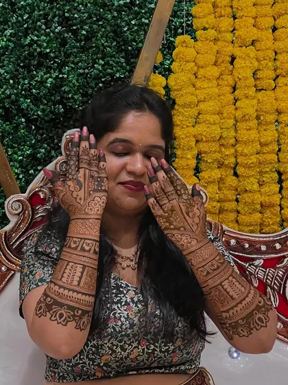 A sweet, candid moment of Madhuri, her hands gently touching her face, showcasing the beautiful henna.