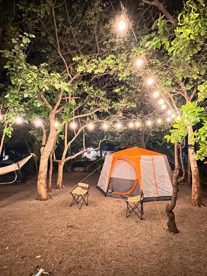 At night, the campsite transforms with beautiful string lights weaving through the trees. This orange tent is ready for guests, complete with camp chairs to relax outside.