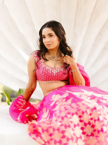 Shree seated against a shell-inspired backdrop, showing off the beautiful flare of her pink Anita Dongre lehenga. A perfect Mehendi look.