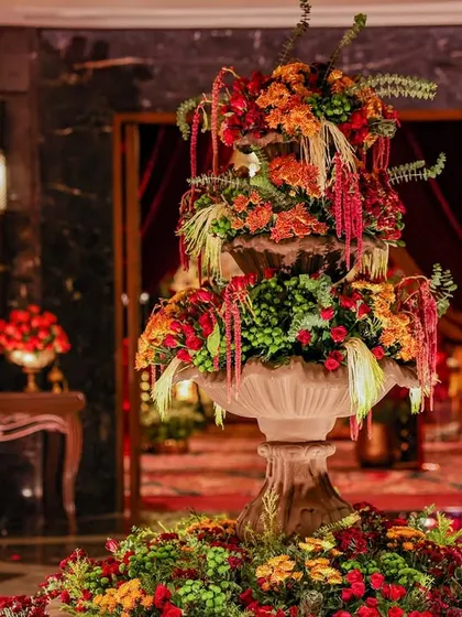 The grand entrance features a magnificent three-tiered floral fountain, overflowing with red, orange, and green blooms. This creates an immediate sense of abundance and celebration for arriving guests.