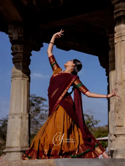 Posing within the magnificent architecture of a South Indian temple. The grandeur of the stone pillars and the open sky creates a breathtaking canvas for a dance portrait.