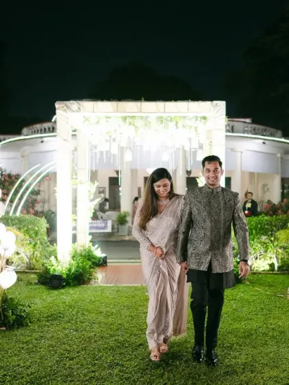 A grand entrance for the happy couple. They walk hand-in-hand through a garden path lined with modern, heart-shaped lights, a beautiful start to their elegant reception.