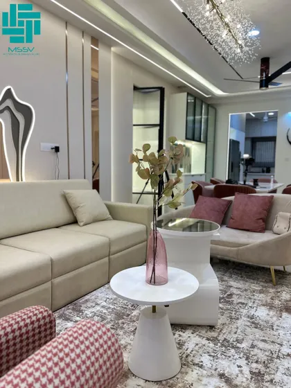A luxurious living room with a beige sofa, pink patterned armchairs, and a stunning crystal-like chandelier. The wall features built-in arched niches for displaying decor.