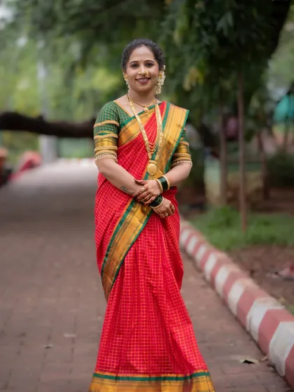 A full-length portrait showcasing the complete traditional attire for Vat Purnima. The classic red and green saree with gold jewelry stands out beautifully against the natural green backdrop of the park.