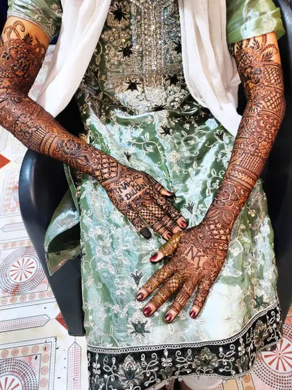 A bride showcasing her full-arm mehndi, which includes personalized text "Nawaz ki Dulhan" (Nawaz's Bride).
