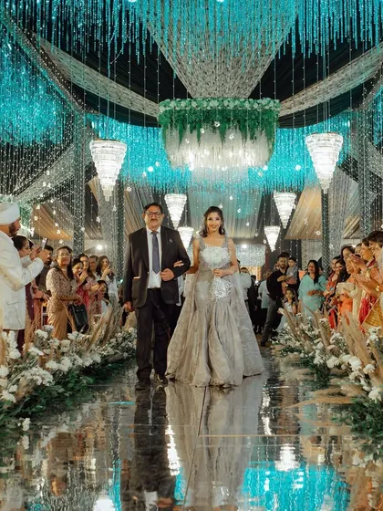 The bride makes her grand entrance, walking down a stunning mirrored aisle with her father, surrounded by guests and beautiful decor.