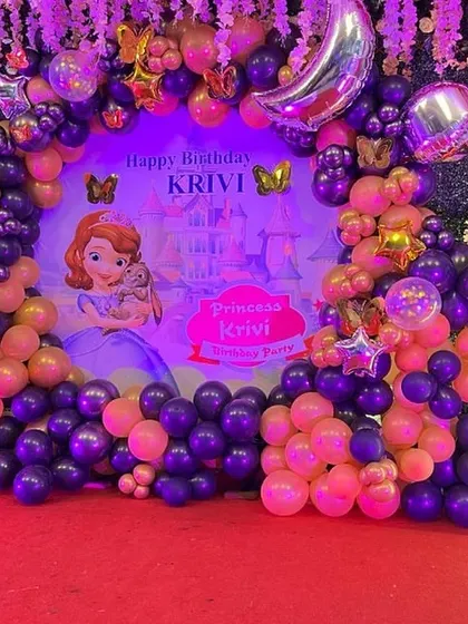 A "Sofia the First" princess theme for a first birthday. This grand setup includes a custom backdrop, a full balloon arch in purple and pink, and a light-up number "1".