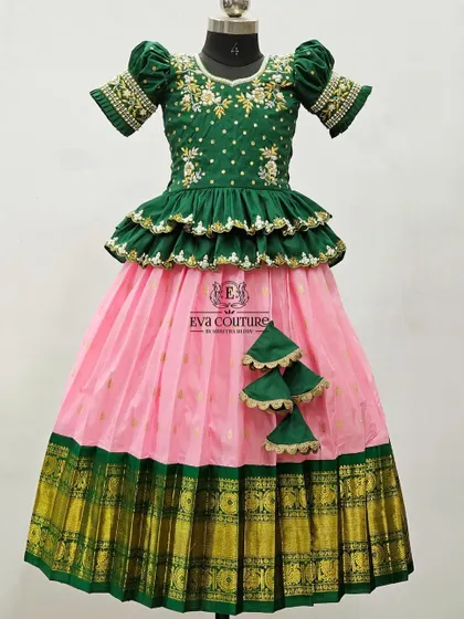 A designer lehenga with a tiered, ruffled peplum top. The dark green blouse has beautiful floral embroidery, and it's paired with a simple pink skirt with a green and gold border.