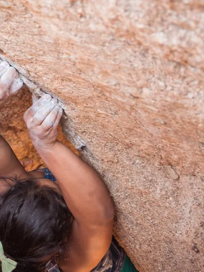 A close-up on a climber's hands finding a crimp hold. This shot details the physical connection and strength required to grip the smallest features of the rock.