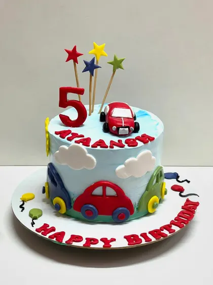 A simple and cute car-themed cake for a 5th birthday. The light blue cake is decorated with colorful fondant cars, clouds, and stars, making it a cheerful and fun design.