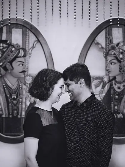 A sweet black and white portrait of a couple, framed by traditional Indian paintings.