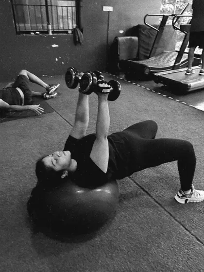 This black and white photo shows a client performing a dumbbell press on a stability ball, an exercise that forces the core to work hard to maintain balance.